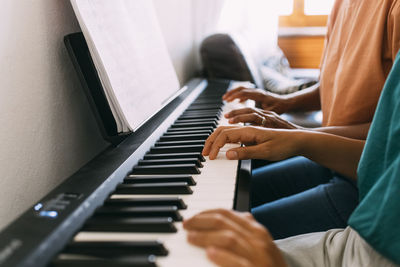 Hands of woman and girl playing piano at home