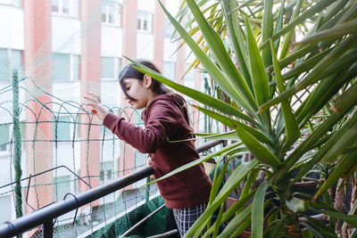 Side view of young girl standing against plants watching outside