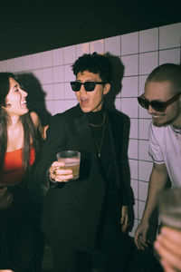 Cheerful non-binary person enjoying dance with friends against wall at nightclub