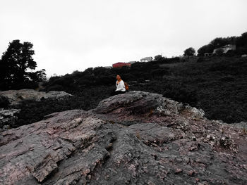 Woman sitting on rock against sky