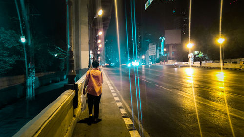 Rear view of man walking on illuminated street at night