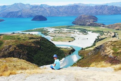 Man sitting on rock by sea against mountains