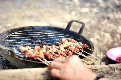 Cropped hand of person cooking meat on barbecue grill