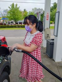 Woman holding camera while standing against cars