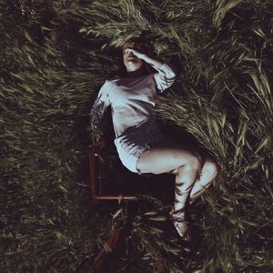 Directly above view of woman lying by wooden chair on grass