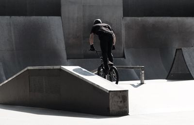 Rear view of man doing stunt on bicycle at skateboard park