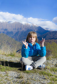 The boy sits in the lotus position and holds his hands up. the mountains. 