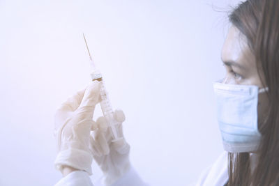 Close-up of doctor wearing mask holding syringe against white background