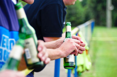 Midsection of men holding beer bottles while standing by railing