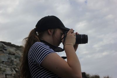 Side view of young woman photographing against sky