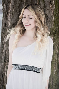 Beautiful young woman standing by tree trunk