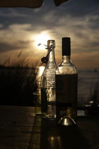 Close-up of bottle against sea during sunset