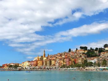 Buildings at waterfront against cloudy sky