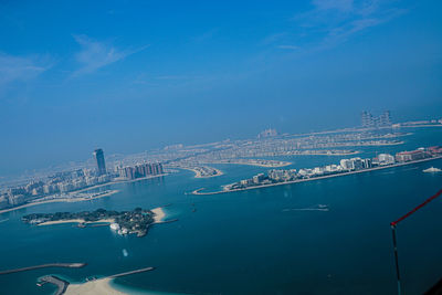 Aerial view of city by sea against blue sky
