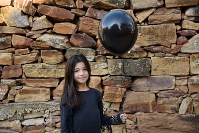 Girl playing with balloon against stone wall