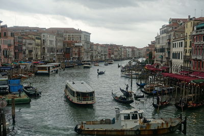 Sailboats moored on canal amidst buildings in city against sky