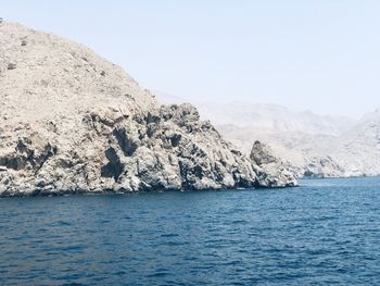 Scenic view of sea by mountain against clear sky