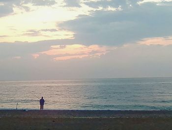 Silhouette man standing on beach against sky during sunset