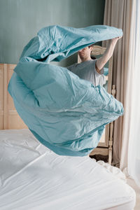 Adult man is putting the bedding cover or mattress pad on the bed. regular bed linen change