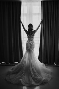 Rear view of bride with arms raised standing by window