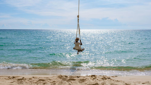 Man swinging on beach against sky