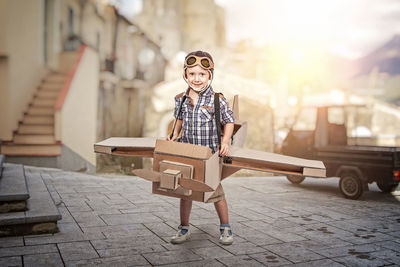 Portrait of boy in cardboard airplane on road against sky