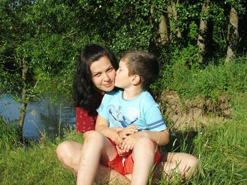 Happy friends sitting on grass against plants