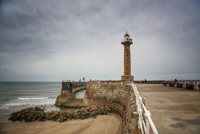 Lighthouse by sea against sky