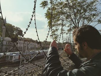 Man looking at railroad tracks through razor wire fence