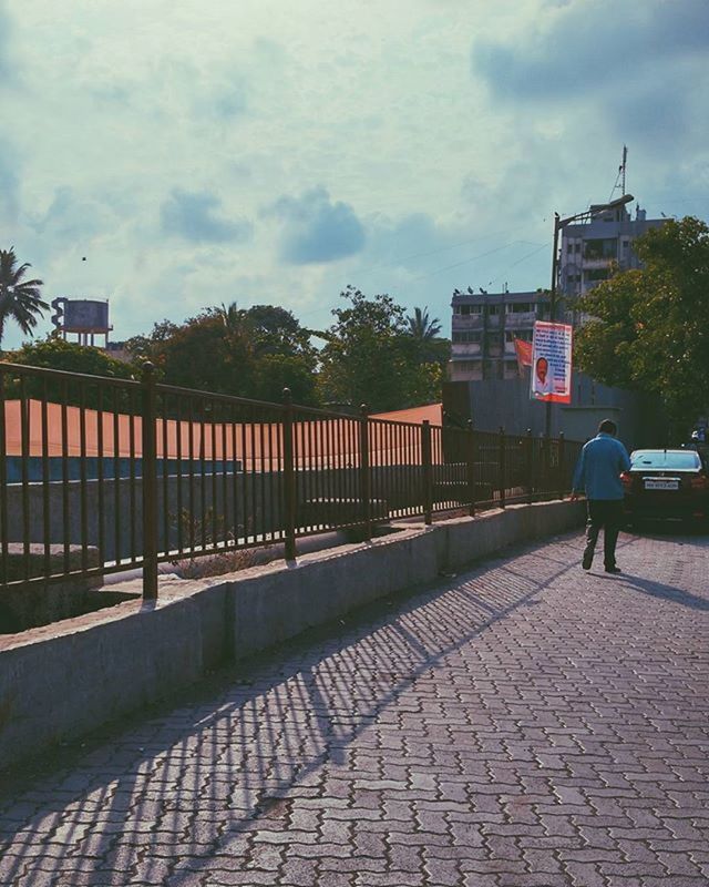 building exterior, sky, architecture, built structure, cloud - sky, men, lifestyles, walking, tree, full length, street, cobblestone, person, leisure activity, city, sidewalk, footpath, cloud