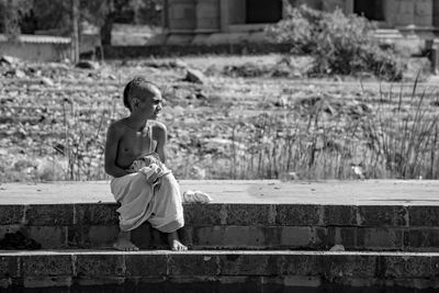 Rear view of shirtless boy sitting on staircase