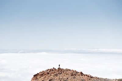 Distant view of person standing on mountain against sky