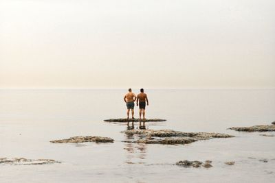 Rear view of friends on beach against clear sky