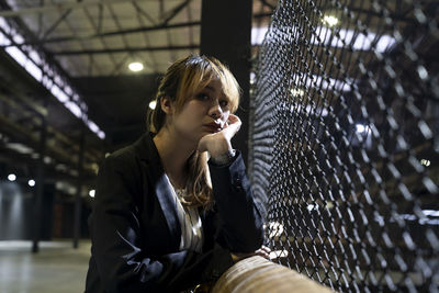 Portrait of sad businesswoman standing by fence at railroad station