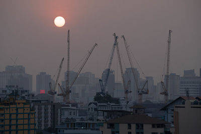 Cranes in city against sky at dusk