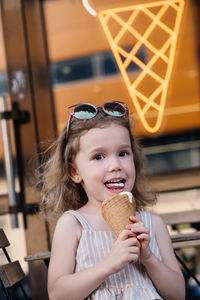 Toddler child eating cone ice cream outside near cafe. cute blonde caucasian girl licking frozen