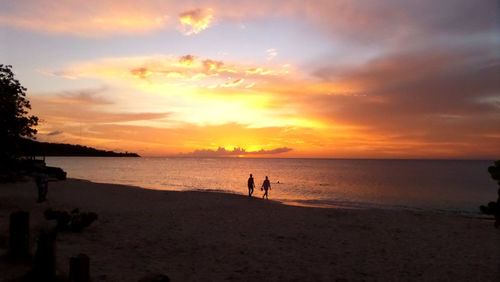 Silhouette of people walking on beach at sunset