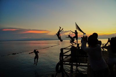 Silhouette people at beach against sky during sunset