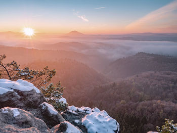 Mountain morning landscape with fog and trees. snowy rocks in foreground