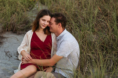 Young pregnant woman with husband sitting and hugging outdoor.