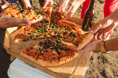 Crop anonymous friends gathering around delicious pizza during summer hangout on sandy beach in costa rica