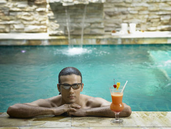 Portrait of shirtless young man wearing sunglasses while swimming in pool