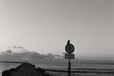 Road sign by sea against clear sky