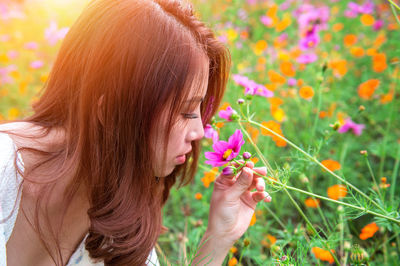 Close-up of young woman smelling cosmos flower at field