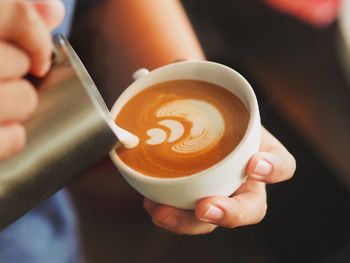 Cropped image of person making froth art on coffee