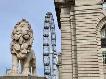 Low angle view of lion statue and millennium wheel by building against clear sky