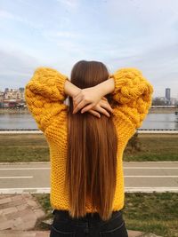 Rear view of young woman with long hair standing against river