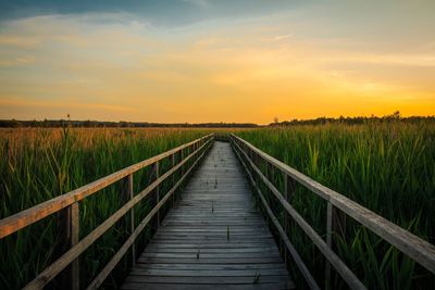 Pier over field against sky during sunset