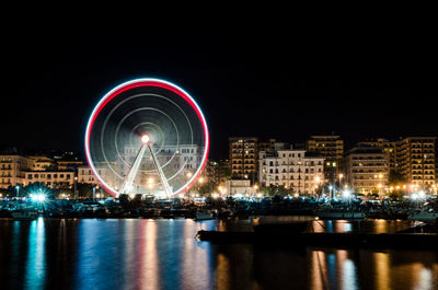 Illuminated ferris wheel in city against clear sky at night