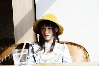 Portrait of beautiful young woman sitting against wall